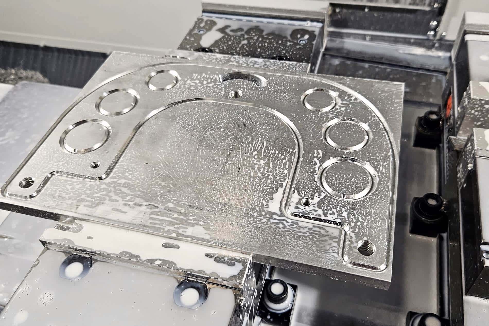 A freshly machined aluminum grinder plate, still wet with coolant, on the HAAS mill table