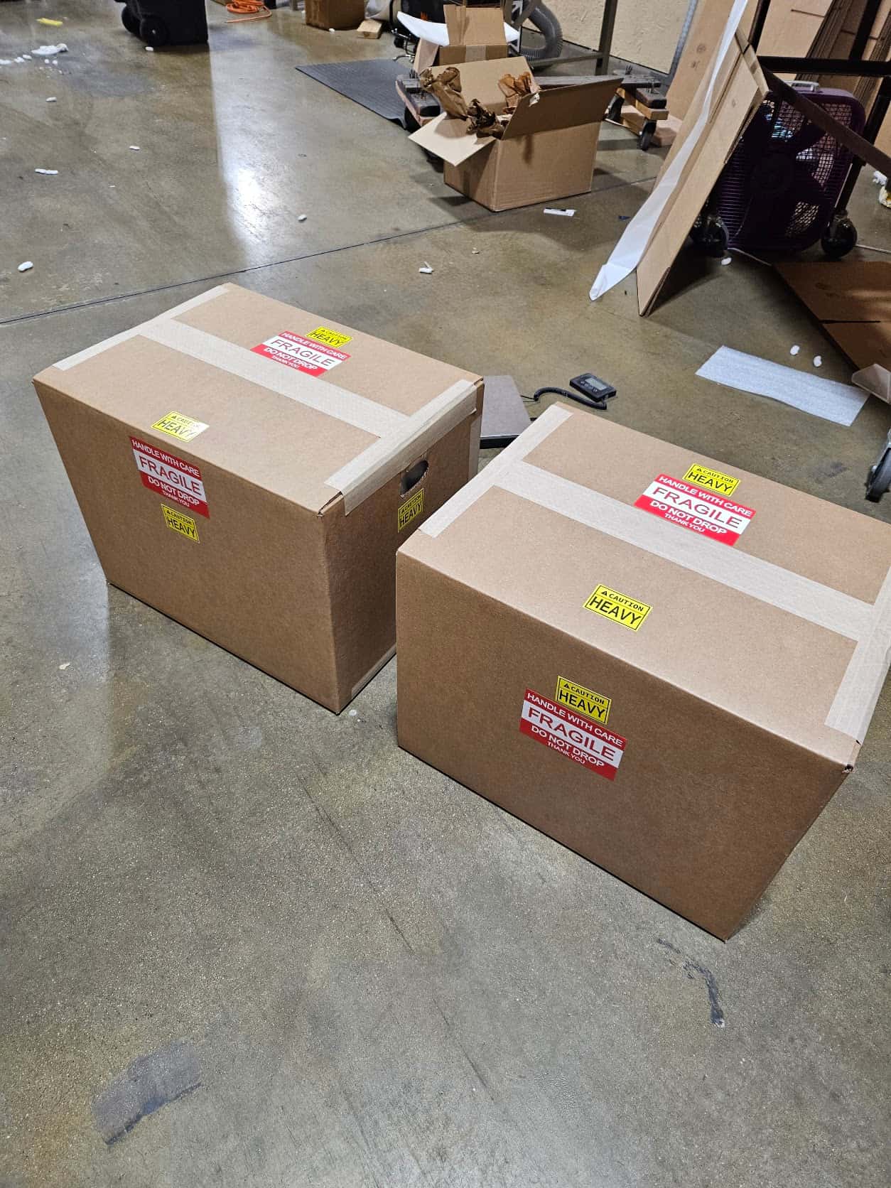 Two finished Torus grinders boxed and taped with FRAGILE and HEAVY labels on the shop floor, ready to ship